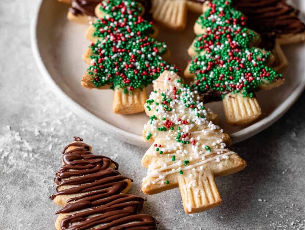 Festive Christmas shortbread trees decorated with green, red, and white sprinkles and drizzled with chocolate.