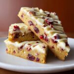 A stack of three delicious Cranberry White Chocolate Blondies, drizzled with white chocolate.