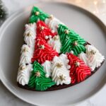 A slice of Frosted Christmas Tree Brownies decorated with red, green, and white frosting, edible pearls, and gold stars.