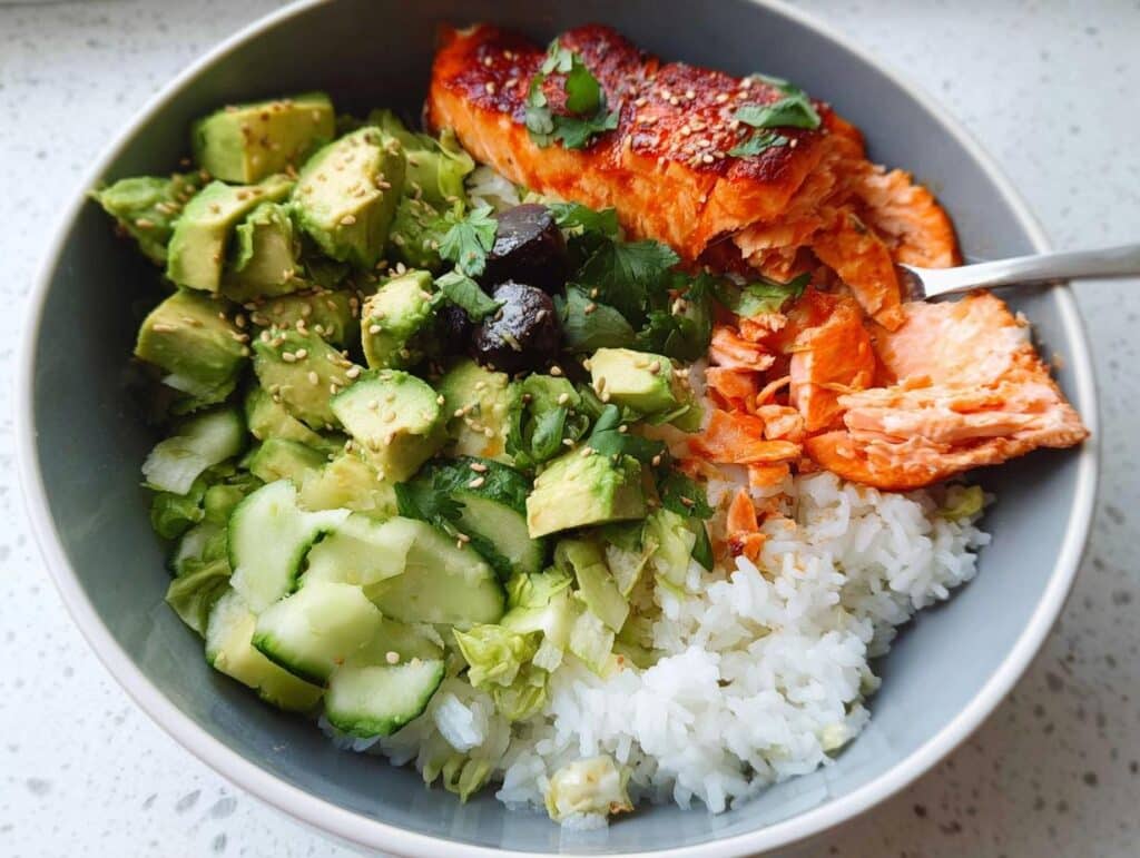 A vibrant Salmon Avocado Protein Bowl featuring flaked salmon, diced avocado, cucumber, and rice.